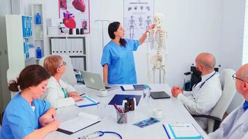sjuksköterska ger presentation i främre av doktorer team handla om mänsklig anatomi använder sig av skelett. klinik expert- terapeut talande med kollegor handla om sjukdom, medicin professionell. video