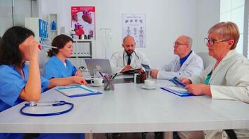 grupo de médico personal que se discute en hospital reunión habitación acerca de paciente radiografía. clínica experto terapeuta hablando con colegas acerca de enfermedad, diagnóstico para pacientes tratamiento cuestiones video