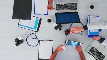 Haut vue de équipe médecins sur bureau table avec stéthoscope et numérique dispositifs ayant conférence. médical groupe travail dans clinique sur copie espace, plat allonger en utilisant moderne technologie. video