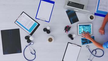 parte superior ver de enfermero analizando humano cerebro utilizando tableta en flatlay sentado en escritorio en clínica con radiografía y digital dispositivos. asistente tomando notas en portapapeles, investigando en Copiar espacio video