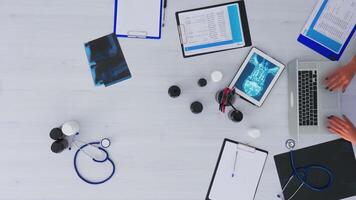 Top view of woman doctor hands typing on laptop sitting on desk with x-ray and medical equipment all around. Assistant working in health clinic using modern devices. Copy space, flat lay concept video