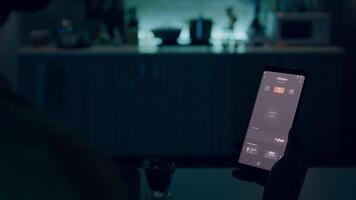 person ser på smartphone med smart Hem lampor app Sammanträde i kök av hus med automatisering belysning systemet, vändning på lökar med röst kommando. hög tech automatiserad programvara video