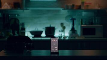 telefon med intelligent programvara placerad på tabell i kök med ingen i, kontrollerande ljus med hög tech Ansökan. mobil med smart Hem app i tömma hus automatisering systemet video