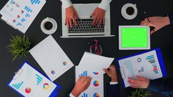 Top view of unrecognisable businessman looking on green screen of tablet during brainstorming in conferance room analysing graphs with coworkers sitting on office table. Copy space, flat lay concept video