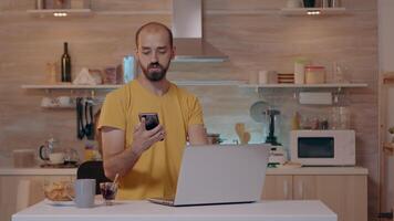 Man working from house with automation lighting system, sitting in kitchen switch off the lights using voice command to smart home application on smartphone. Person controlling light with wifi gadget video