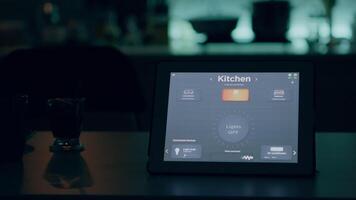 Close up of tablet with wireless lighting automation software placed on kitchen desk in empty house with smart system, turning on lights. Notepad with high tech app controlling electricity effiency video