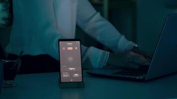 kvinna skriver på bärbar dator Sammanträde i Hem med automatisering belysning systemet använder sig av röst kontrollerade på smartphone vändning på lökar. högtalare grej svarar till kommandon, person kontrollerande atmosfär ljus video