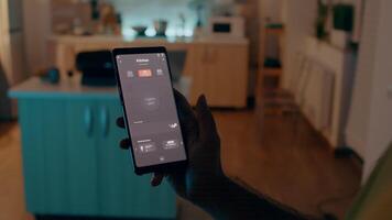 persoon zittend in huis met automatisering licht systeem Holding smartphone draaien Aan bollen, controlerend draadloze kamer sfeer met slim huis sollicitatie. mobiel met modern software app video