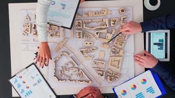 Top view of businesspeople team of architects with buildings prototype, gadgets and papers working at office table. Engineers brainstorming using modern device on copy space, flat lay concept video