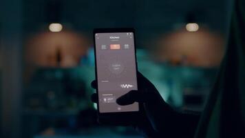 homme en portant téléphone intelligent avec actif intelligent Accueil application commutation sur lumière. la personne tapoter sur écran pour tournant sur le lumières dans maison avec automatisation éclairage système départ à travail à portable video