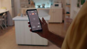 man vändning på lökar i smart hus med automatisering belysning systemet använder sig av röst aktiverad Ansökan innehav smartphone. person kontrollerande lampor i hus med modern programvara innan Start arbetssätt video