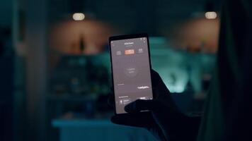 man använder sig av smartphone med smart Hem säkerhet app vändning på de lampor av hus med automatisering belysning systemet. ung person växlande på Glödlampa med trådlös programvara kontrollerande effektivitet av energi video