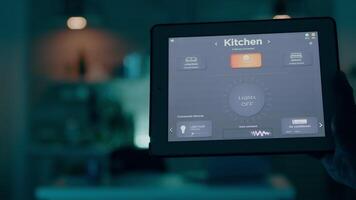 Man holding tablet with lighting control application, turning on the lights sitting in kitchen house with automation lighting system. Person using high technology software working remote at laptop video