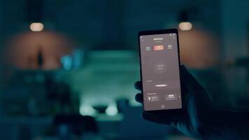 stänga upp av man hand innehav telefon med modern programvara kontrollerande lampor i hus med automatisering belysning systemet, vändning på Glödlampa. person ser på intelligent grej Sammanträde kök av smart Hem video