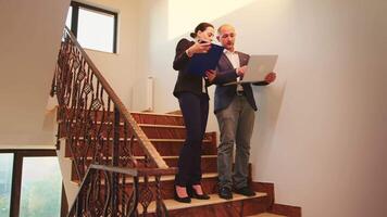 Corporate executive manager holding laptop talking with businesswoman on staircase of business building. Professional successful entrepreneur in team working overtime in modern office video