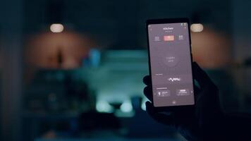 Close up of phone with high tech software lighting controller turning on the light before man working on laptop. Person tapping on screen for switching on the bulb in house with automation system video