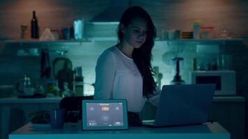 kvinna använder sig av röst aktiverad smart trådlös belysning app på läsplatta vändning på de lökar i hus med modern programvara arbetssätt på bärbar dator. person kontrollerande atmosfär ljus med framtida teknologi video