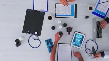 Top view of fast forward shot of doctors having medical conference sitting on desk using digital technology, taking notes, researching and checking appointments. Copy space flat lay time lapse concept video