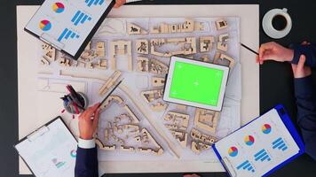 Top view of close up architecture businesspeople working in boardroom meeting, discussing architectural plans for new sustainable shared office looking on greenscreen tablet. Notebook with chroma key video