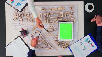 hommes d'affaires et architectes travail avec ville prototype et vert écran tablette pour Nouveau Commencez. Créatif équipe de ingénieurs avec des ordinateurs, schème et carnet avec chrominance clé à bureau. video