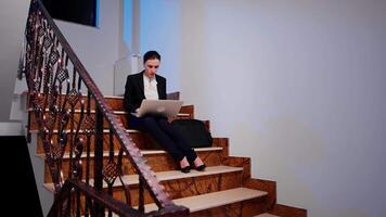 Exhausted overworked entrepreneur doing overtime on project deadline typing on laptop. Serious entrepreneur working on corporate job sitting on staircase of business building late at night. video