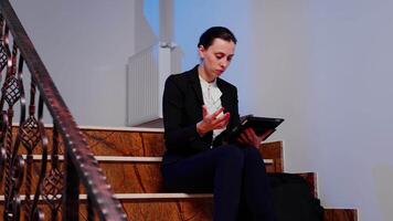 Worried stressed company manager reading from tablet deadline of finacial business project sitting on staircase of business building. Serious entrepreneur working on corpotare job late at night. video