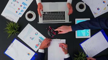 Directly above shot of businesspeople sitting at office desk and discussing financial documents using digital devices. Teamworkers planning in conference room on copy space, flat lay concept. video