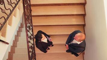 Haut vue de les partenaires réunion sur escaliers dans la finance entreprise entreprise tremblement mains et en parlant. équipe de professionnel hommes d'affaires travail ensemble dans moderne financier bâtiment salutation. video