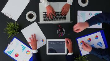 Top view of office workers discussing business financial diagrams and working on digital devices. Working in team conference with project planning document and modern technology on company table. video