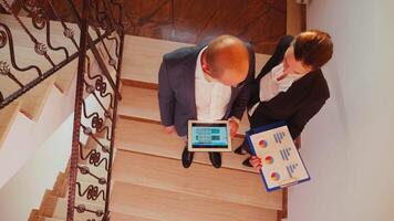 topp se av kollegor läsning årlig rapporter använder sig av läsplatta och dokument stående på trappa av företag byggnad. grupp av professionell framgångsrik affärsmän arbetssätt i modern finansiell arbetsplats video