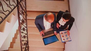 Top view of businessman holding laptop discussing with office colleague on staircase of business building. Group of professional successful businesspeople working in modern financial workplace. video