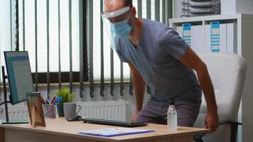 Freelancer wearing protection face mask cleaning hands with sanitizer gel at workplace. Entrepreneur working in new normal office disinfecting using antibacterial alcohol against corona virus. video