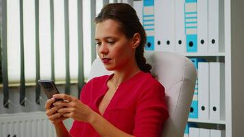 Close up of woman chatting using phone in office room. Hispanic entrepreneur working in professional workspace, workplace in personal corporate company typing on mobile phone in front of computer. video