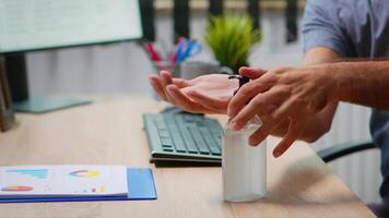 fechar acima do homem usando antibacteriano gel antes escrevendo em computador. empreendedor trabalhando dentro Novo normal companhia escritório local de trabalho limpeza desinfecção mãos usando higienizar álcool contra corona vírus. video