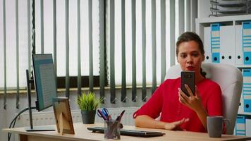 Hispanic lady having virtual meeting using phone sitting on modern office. Freelancer working with business remotely team discussing chatting having online conference, webinar with internet technology video