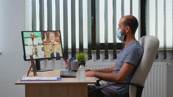 Freelancer making a conference with face mask in modern office room. Entrepreneur working in new normal workplace having online meeting, webinar with remotely team using internet technology video