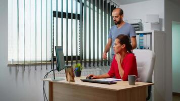 Man explaining solution of problem to hispanic colleague in front of pc. Team working in professional workplace in personal corporate company typing on computer keyboard looking pointing at desktop video