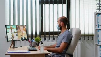 Freelancer with face mask speaking at virtual meeting with team. Entrepreneur working with business remotely coworkers discussing chatting having online conference webinar using internet technology video