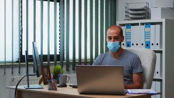 Man using laptop discussing project online wearing protective mask. Freelancer working in new normal office workplace chatting talking having virtual conference, meeting, using internet technology video