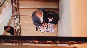 Top view of businesspeople holding clipboards looking on graphs and talking standing on stairs. Colleague entrepreneur working together in evening at corporate job explaining difficult project. video