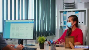 People wearing face masks back at work in office with new normal. Team working in workspace in personal corporate company typing on computer keyboard looking at desktop respecting social distancing. video