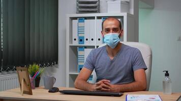 Worker wearing protective face mask and talking on camera about company problems during coronavirus. Pov of entrepreneur working in new normal workplace having online meeting, with remotely team video