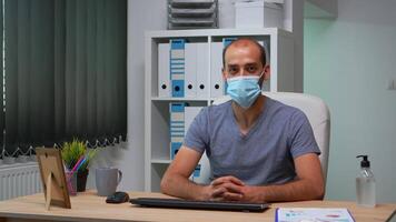 Freelancer on job talking on camera with prrotection face mask. Pov of entrepreneur working in new normal workplace having online meeting, webinar with business remotely team using internet technology video
