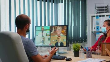 Man with protection mask participating at online group conference in new normal office. Freelancer working in workplace chatting talking having virtual meeting, using internet technology video