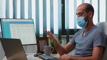 Man with protective mask during meeting sitting alone in office. Freelancer working in new normal workplace chatting talking having virtual conference, webinar, using internet technology video