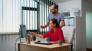 Team searching the best solution in front of computer in modern office room. Coworkers discussing working in workplace in personal corporate company typing on pc keyboard pointing at desktop video