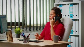 Employee talking on phone in business modern office. Hispanic entrepreneur working in professional workspace, workplace in personal corporate company speaking on smartphone looking at computer desktop video