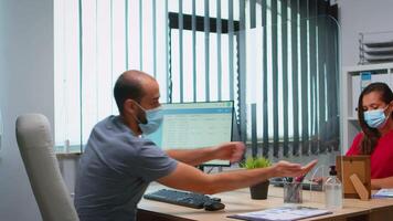 hombre y mujer vistiendo protector cara máscara y acuerdo distancia a evitar codicioso virus en empresa lugar de trabajo trabajando en oficina con nuevo normal. compañeros de trabajo utilizando desinfectar alcohol gel en contra corona virus video