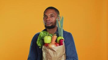 Young adult accidentally dropping an apple from his paper bag full of ethically sourced fruits and veggies, buying a variety of organic homegrown goods. Support vegan lifestyle. Camera A. video