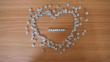 felicidad - palabras desde alfabeto blanco rosario bloques con letras en corazón, aleatorio letras alrededor, parte superior ver de madera antecedentes foto